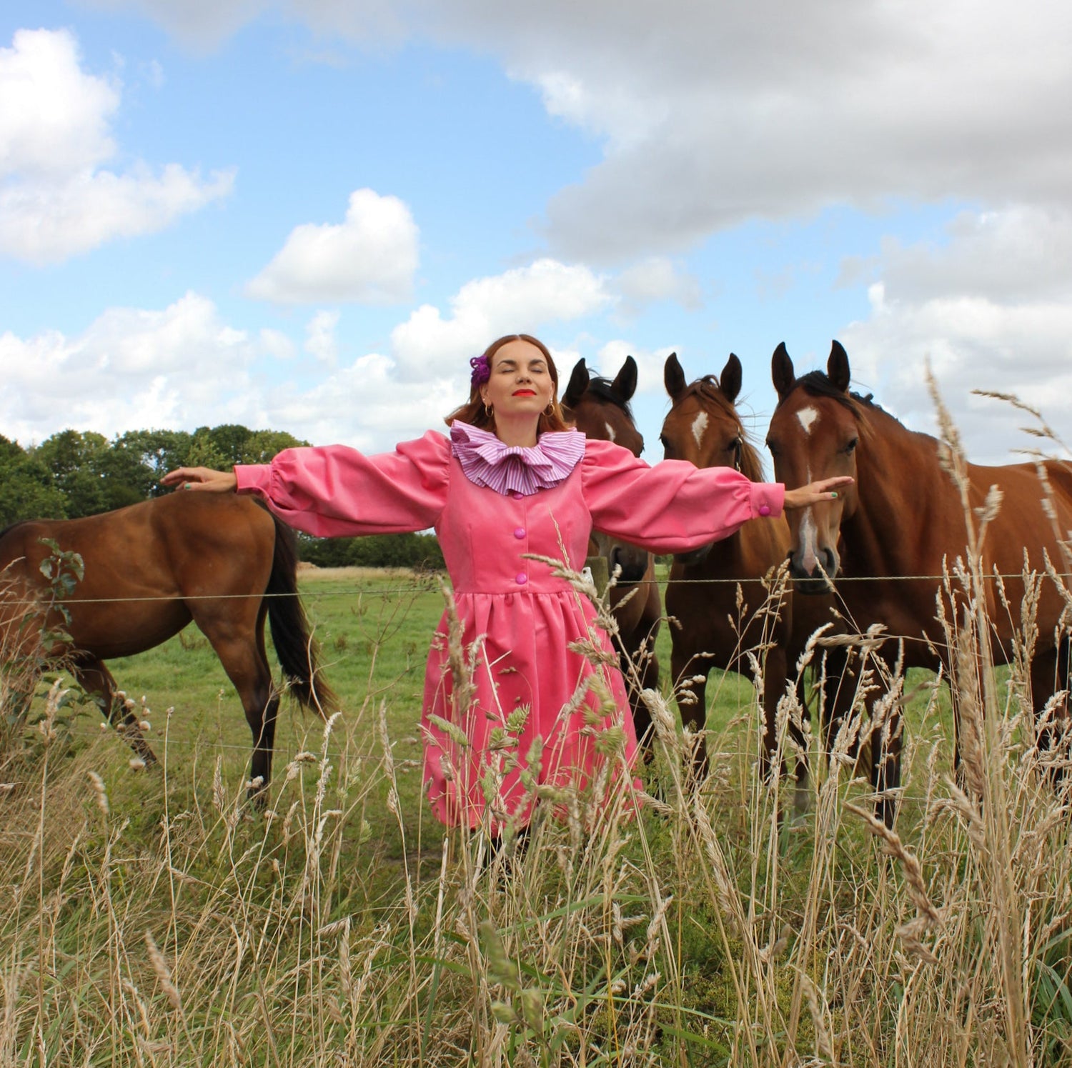 Woman in a pink dress standing in a field with horses